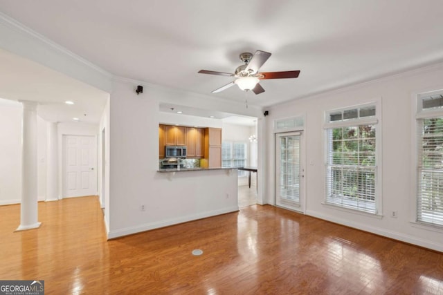 unfurnished living room featuring ornate columns, a wealth of natural light, ornamental molding, and ceiling fan