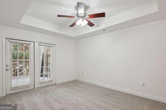 carpeted empty room with ceiling fan and a tray ceiling