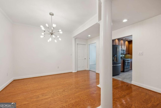 unfurnished room with an inviting chandelier, ornate columns, and light hardwood / wood-style flooring