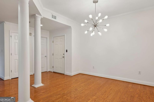 empty room with light hardwood / wood-style floors, an inviting chandelier, decorative columns, and crown molding