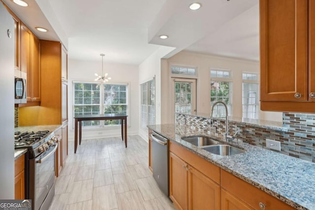 kitchen featuring pendant lighting, sink, appliances with stainless steel finishes, a notable chandelier, and light stone counters