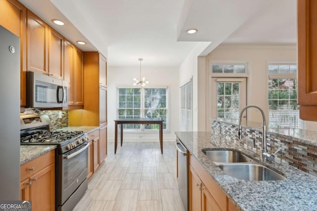 kitchen with light stone countertops, stainless steel appliances, hanging light fixtures, and sink