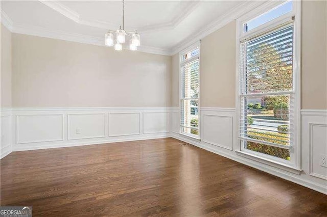 empty room featuring a raised ceiling, ornamental molding, dark hardwood / wood-style floors, and an inviting chandelier