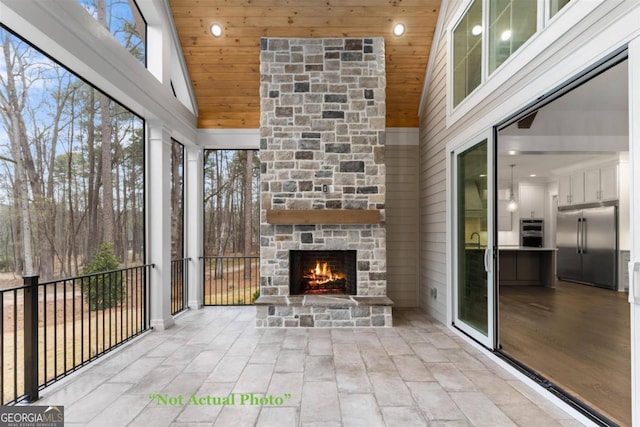 unfurnished sunroom with vaulted ceiling, wood ceiling, and an outdoor stone fireplace