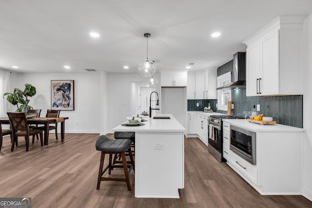 kitchen featuring white cabinets, wall chimney exhaust hood, stainless steel appliances, an island with sink, and sink