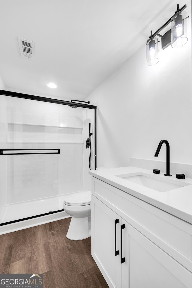 bathroom with toilet, vanity, a shower with shower door, and hardwood / wood-style flooring