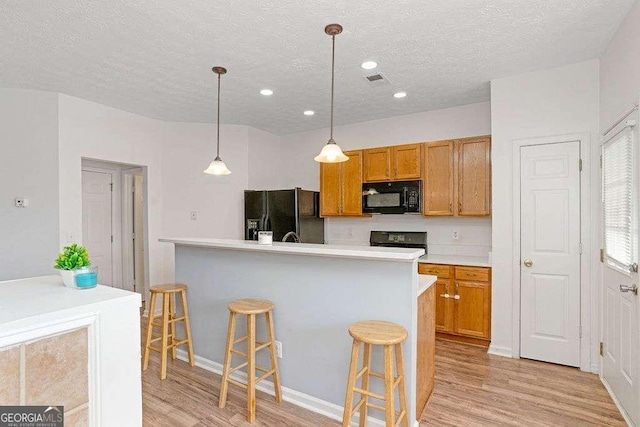 kitchen featuring a kitchen bar, a textured ceiling, black appliances, pendant lighting, and light hardwood / wood-style flooring