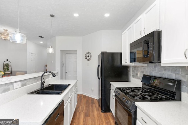 kitchen with a sink, white cabinets, light countertops, black appliances, and pendant lighting