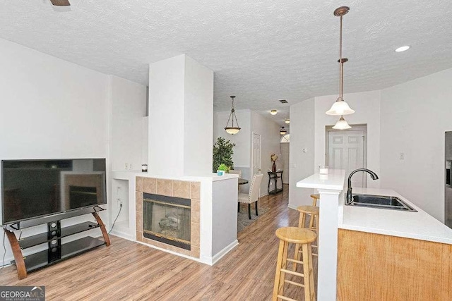 interior space featuring a tile fireplace, sink, hanging light fixtures, a textured ceiling, and light wood-type flooring