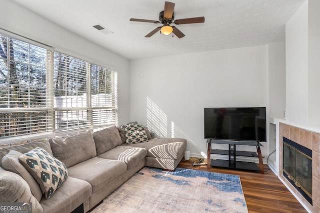 living room featuring baseboards, visible vents, dark wood finished floors, a ceiling fan, and a tile fireplace