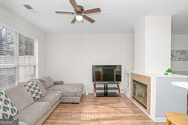 living room featuring a textured ceiling, light hardwood / wood-style floors, ceiling fan, and a tiled fireplace