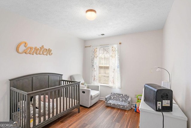 bedroom with dark wood-style floors, a crib, a textured ceiling, and visible vents