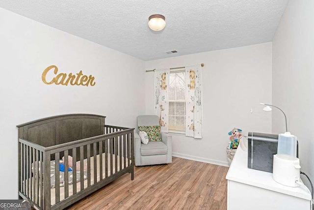 bedroom featuring hardwood / wood-style flooring, a crib, and a textured ceiling