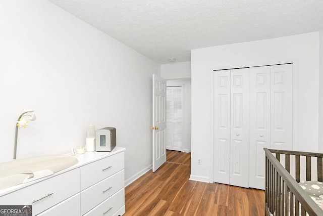 unfurnished bedroom featuring dark wood-style floors, a closet, a textured ceiling, and baseboards