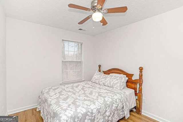 bedroom with ceiling fan, light hardwood / wood-style flooring, and a textured ceiling