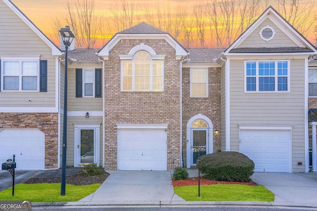 multi unit property featuring an attached garage, a shingled roof, concrete driveway, and brick siding