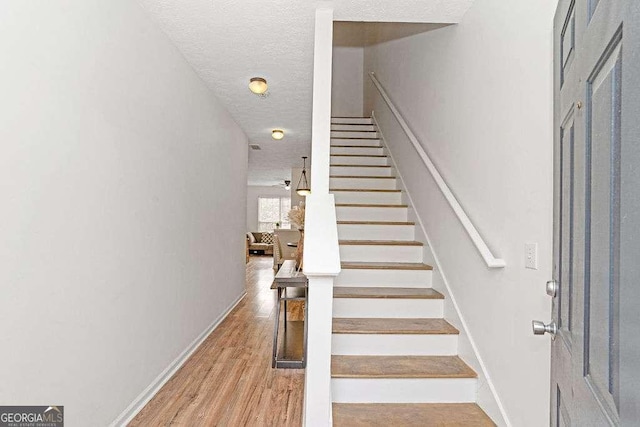 stairs with a textured ceiling, wood finished floors, and baseboards