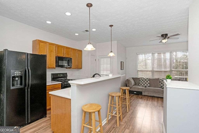 kitchen with black appliances, ceiling fan, a textured ceiling, light hardwood / wood-style floors, and a breakfast bar area