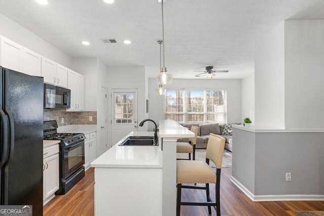 kitchen featuring a sink, hanging light fixtures, light countertops, black appliances, and an island with sink