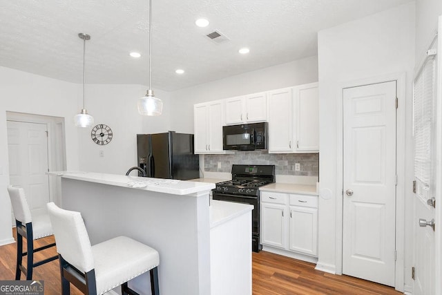 kitchen featuring an island with sink, a breakfast bar area, light countertops, black appliances, and white cabinetry