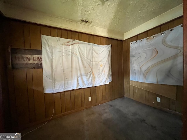 carpeted empty room featuring a textured ceiling and wooden walls