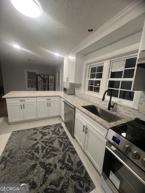 kitchen with appliances with stainless steel finishes, white cabinetry, sink, light stone counters, and kitchen peninsula