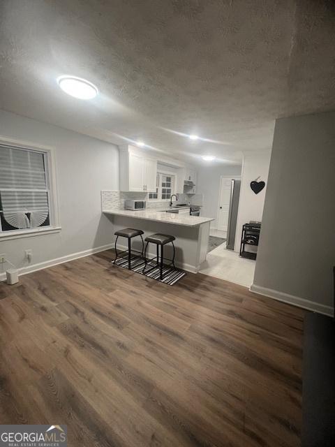 kitchen featuring white cabinetry, a kitchen breakfast bar, light hardwood / wood-style floors, a textured ceiling, and kitchen peninsula