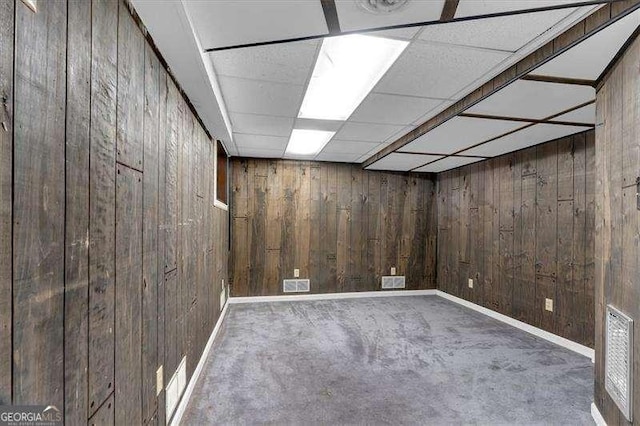 basement with carpet flooring, a paneled ceiling, and wooden walls