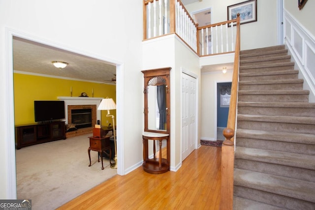 stairway with a towering ceiling, a fireplace, ornamental molding, and wood-type flooring