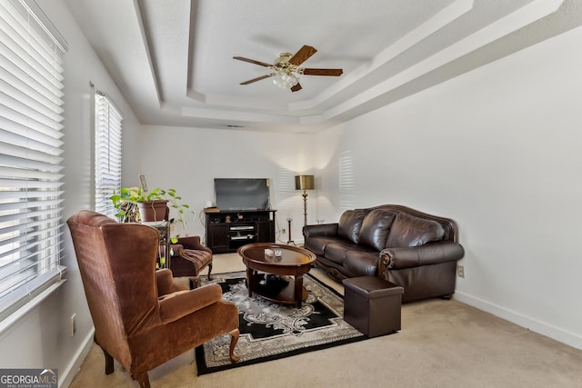 living room with a raised ceiling, ceiling fan, and light colored carpet