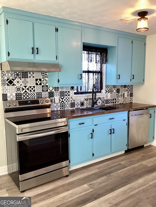 kitchen with sink, blue cabinets, light hardwood / wood-style floors, a textured ceiling, and appliances with stainless steel finishes