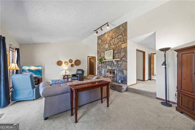 carpeted living room featuring a textured ceiling, a stone fireplace, rail lighting, and vaulted ceiling