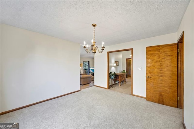 carpeted empty room with a textured ceiling and an inviting chandelier