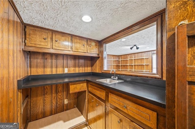 bar featuring a textured ceiling, wood walls, and sink