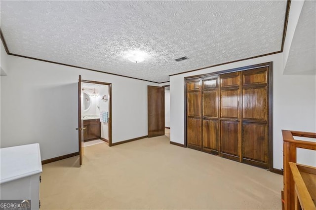 unfurnished bedroom with a textured ceiling, ornamental molding, light carpet, and ensuite bath