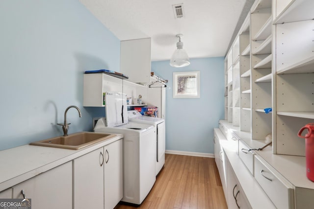 laundry area with light hardwood / wood-style flooring, sink, separate washer and dryer, and cabinets