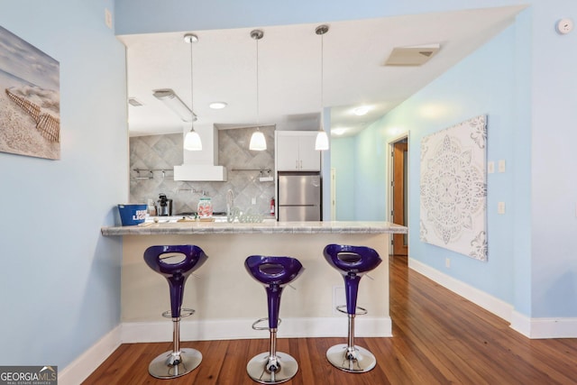 kitchen with a breakfast bar area, stainless steel fridge, white cabinetry, and pendant lighting