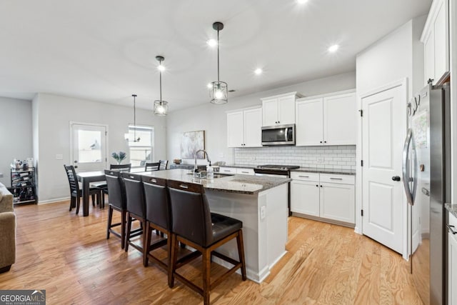 kitchen with pendant lighting, a center island with sink, a kitchen breakfast bar, sink, and stainless steel appliances