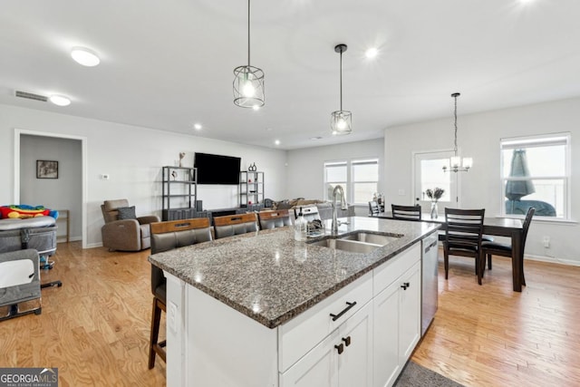 kitchen with white cabinets, sink, dark stone countertops, light wood-type flooring, and an island with sink