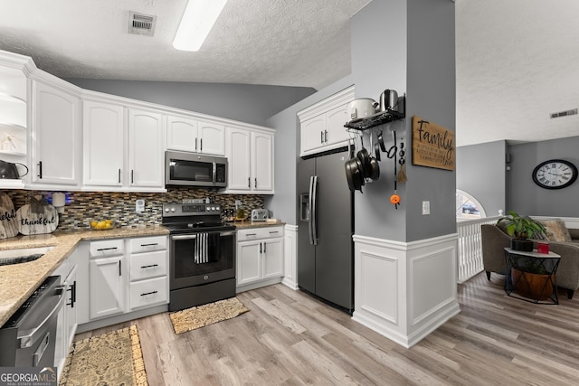 kitchen with stainless steel appliances, light stone countertops, white cabinets, and light hardwood / wood-style flooring