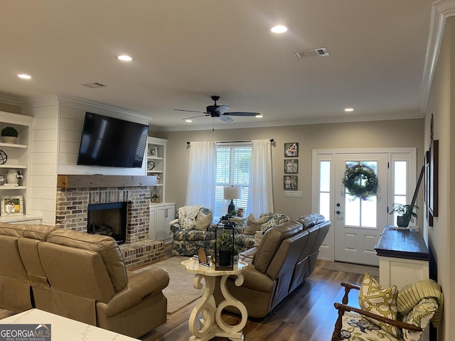 living room with ceiling fan, a fireplace, ornamental molding, and dark wood-type flooring