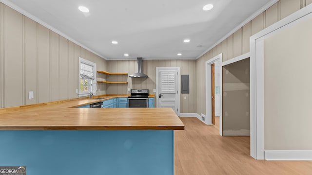 kitchen with wooden counters, appliances with stainless steel finishes, kitchen peninsula, ornamental molding, and wall chimney range hood