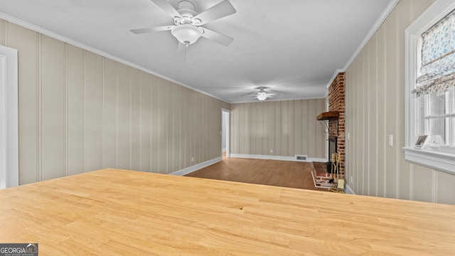 unfurnished room with ceiling fan, a healthy amount of sunlight, crown molding, and a brick fireplace