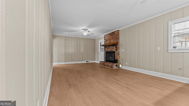 unfurnished living room featuring crown molding, ceiling fan, light wood-type flooring, and a brick fireplace