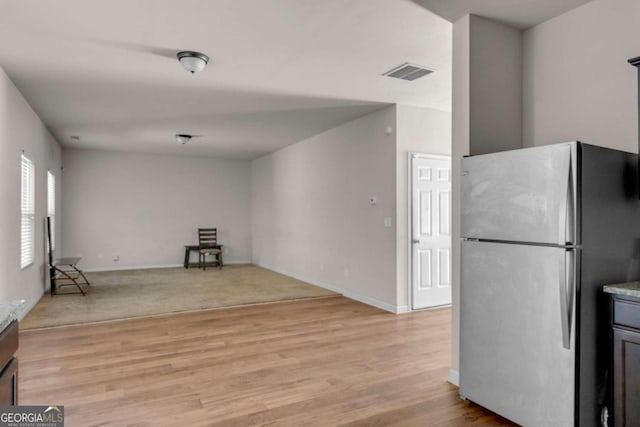 kitchen with stainless steel refrigerator, light stone countertops, and light hardwood / wood-style floors