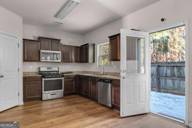 kitchen with light stone counters, sink, light hardwood / wood-style flooring, and appliances with stainless steel finishes