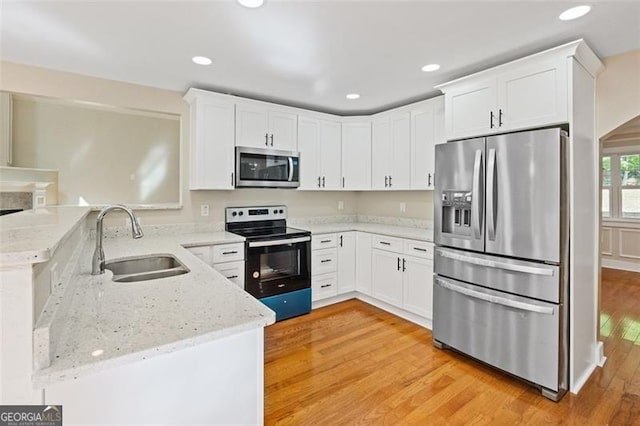 kitchen featuring sink, light stone counters, kitchen peninsula, white cabinets, and appliances with stainless steel finishes