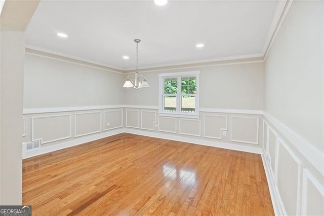 empty room with a notable chandelier, crown molding, and light hardwood / wood-style flooring