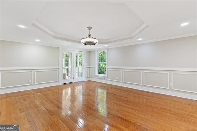 empty room featuring a tray ceiling, crown molding, and light hardwood / wood-style floors