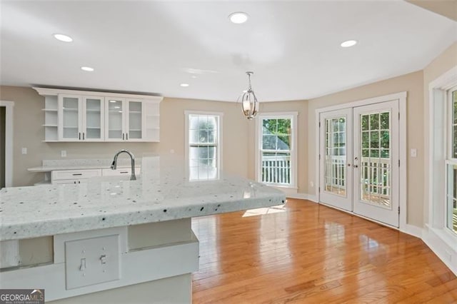 kitchen with french doors, light stone counters, decorative light fixtures, light hardwood / wood-style flooring, and white cabinetry